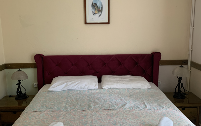 Yatak odası: bordo kapitone başlıklı çift kişilik yatak, iki yanda ahşap komodin ve abajur, duvarda çerçeveli resim.